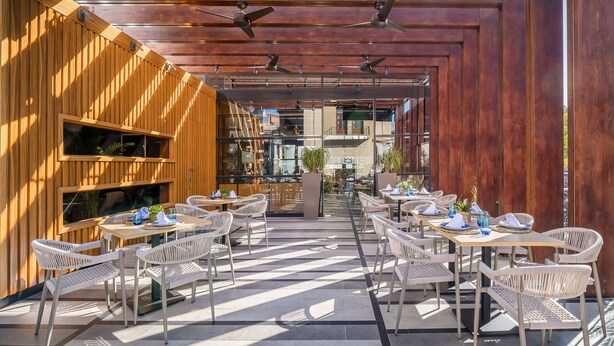 Un área de comedor al aire libre con paneles de madera y sillas de mimbre blanco, con un diseño moderno y vistas al interior.
