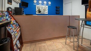 Un área de recepción con pared azul, un reloj, un televisor y un mostrador con una cafetera.