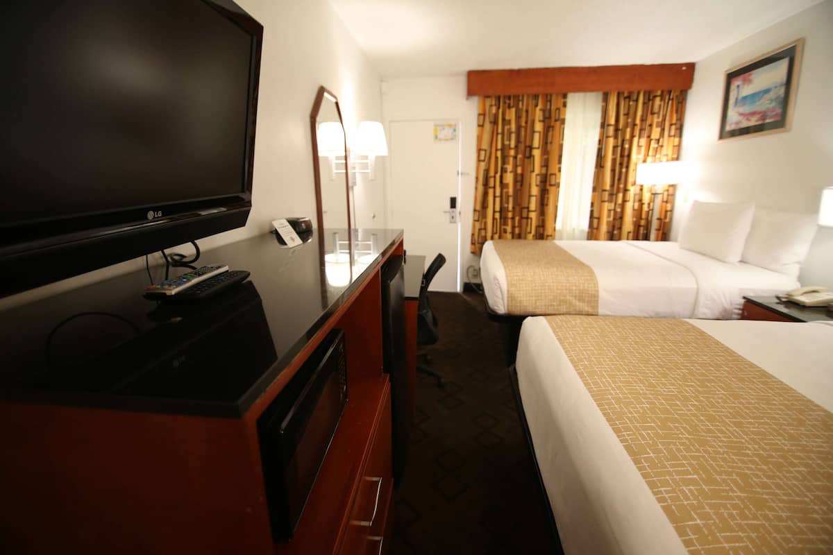 A hotel room with a bed, a TV, a desk with a lamp, and a bathroom door.