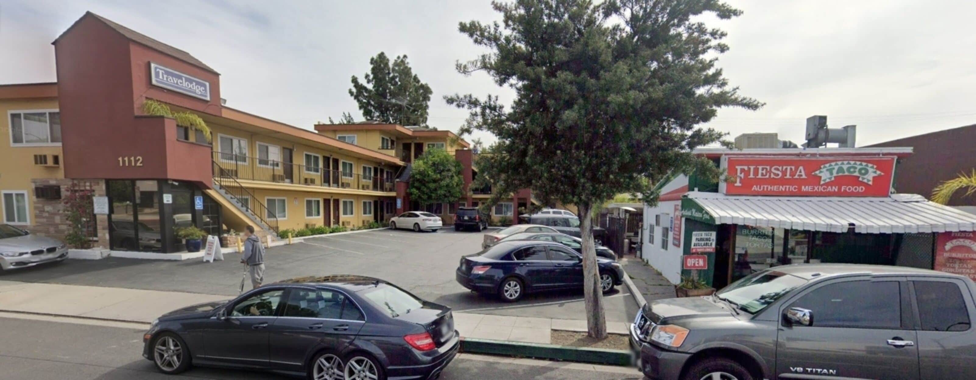 A Travelodge hotel with a parking lot, a Fiesta Taco restaurant, and a V8 Titan SUV parked nearby.