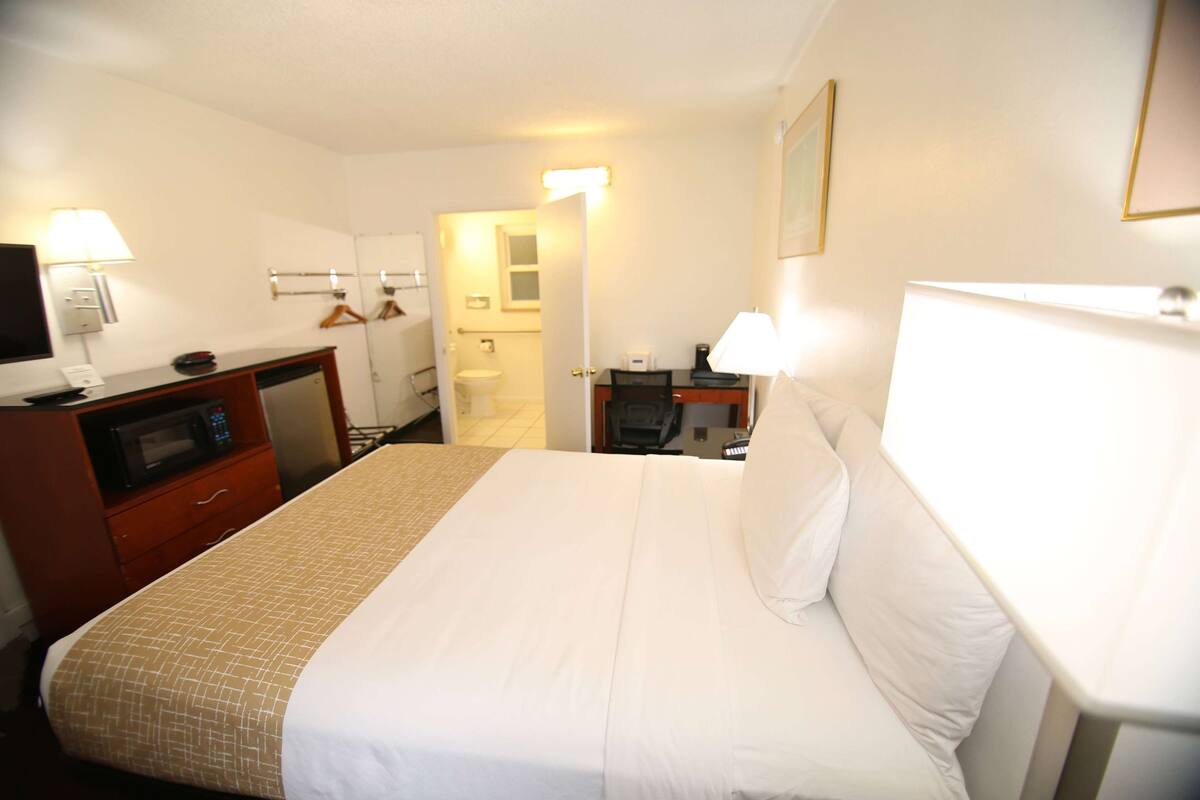 A hotel room with a bed, a desk with a lamp, a microwave, and a TV.