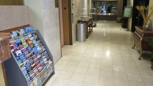 Een hotel lobby met een tijdschriftenrek, een prullenbak, een receptiebalie en een plant.