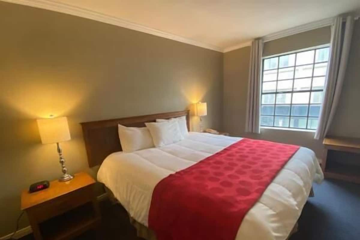 Une chambre d’hôtel avec un lit, des lampes de chevet, une table de nuit et une fenêtre avec des rideaux.