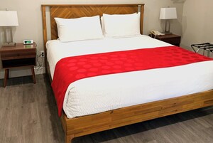 A neatly made bed with a red and white bedspread, a wooden headboard, two bedside tables with lamps, and a nightstand with a phone.
