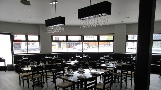 Een restaurantinterieur met meerdere tafels en stoelen, grote ramen en hangende lampen.