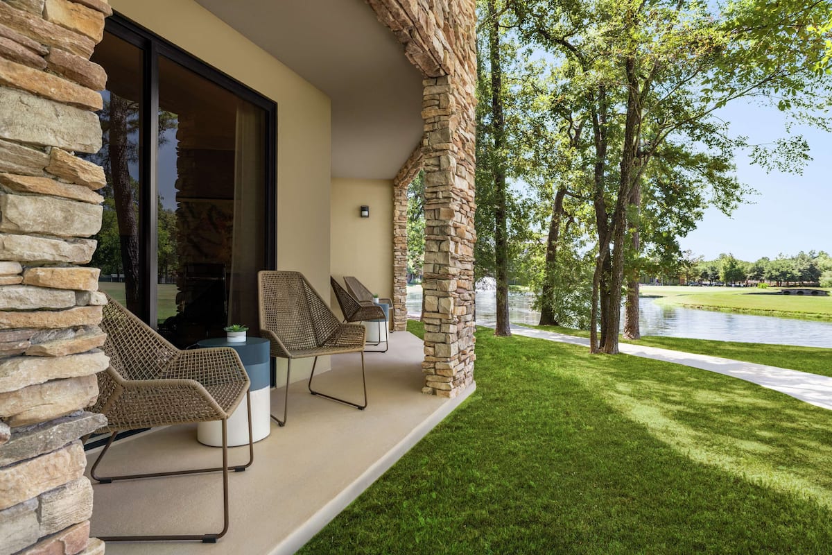 A patio with stone pillars, wicker chairs, and a view of a lake.
