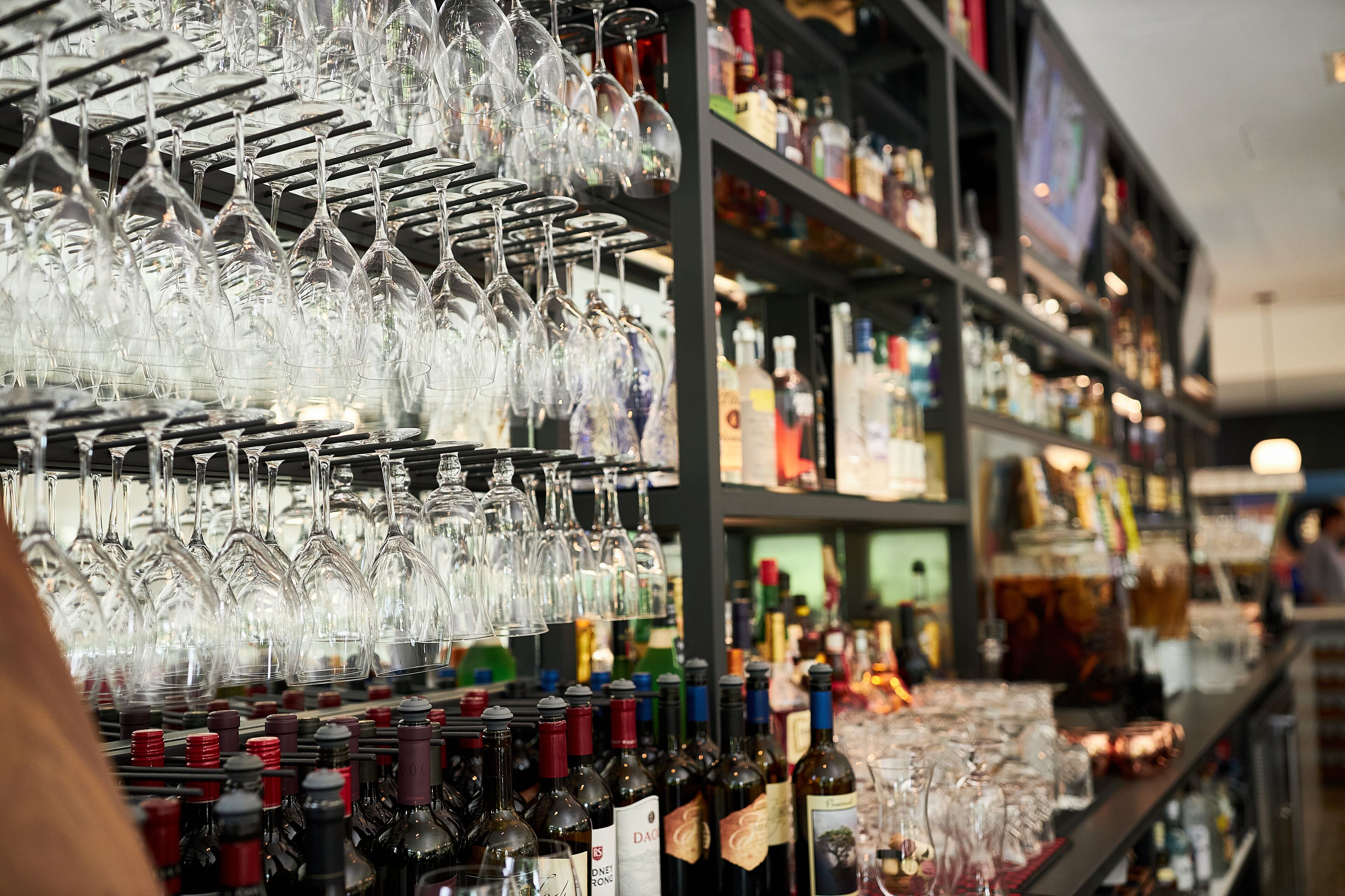 A bar area with shelves stocked with wine bottles and a rack of wine glasses.