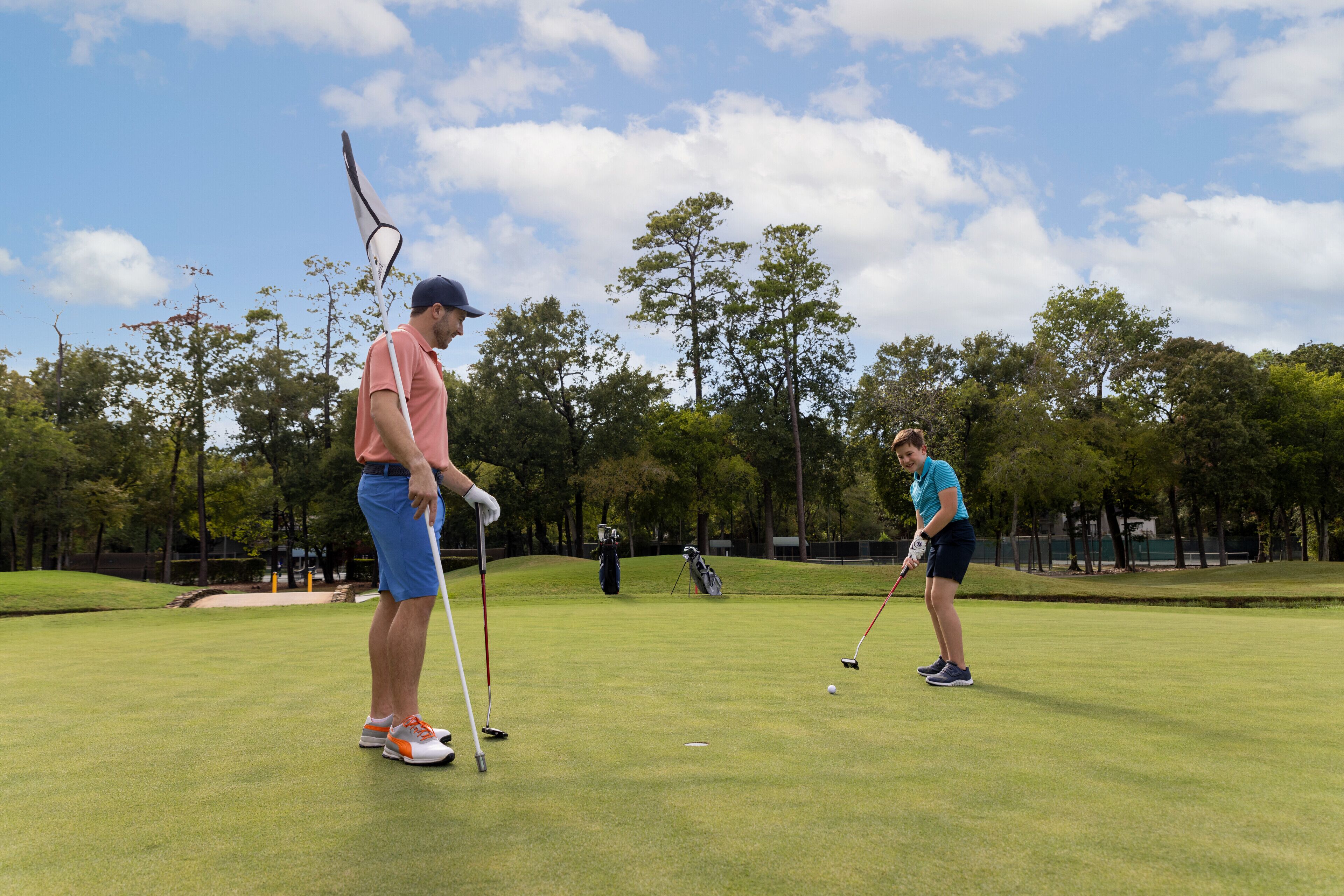 A golf course with two players, one holding a golf club and the other preparing to putt.