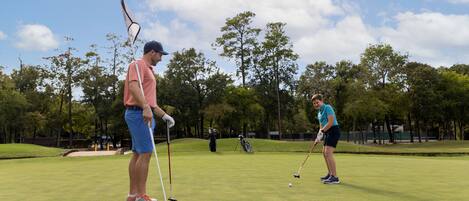 A golf course with two players, one holding a golf club and the other preparing to putt.