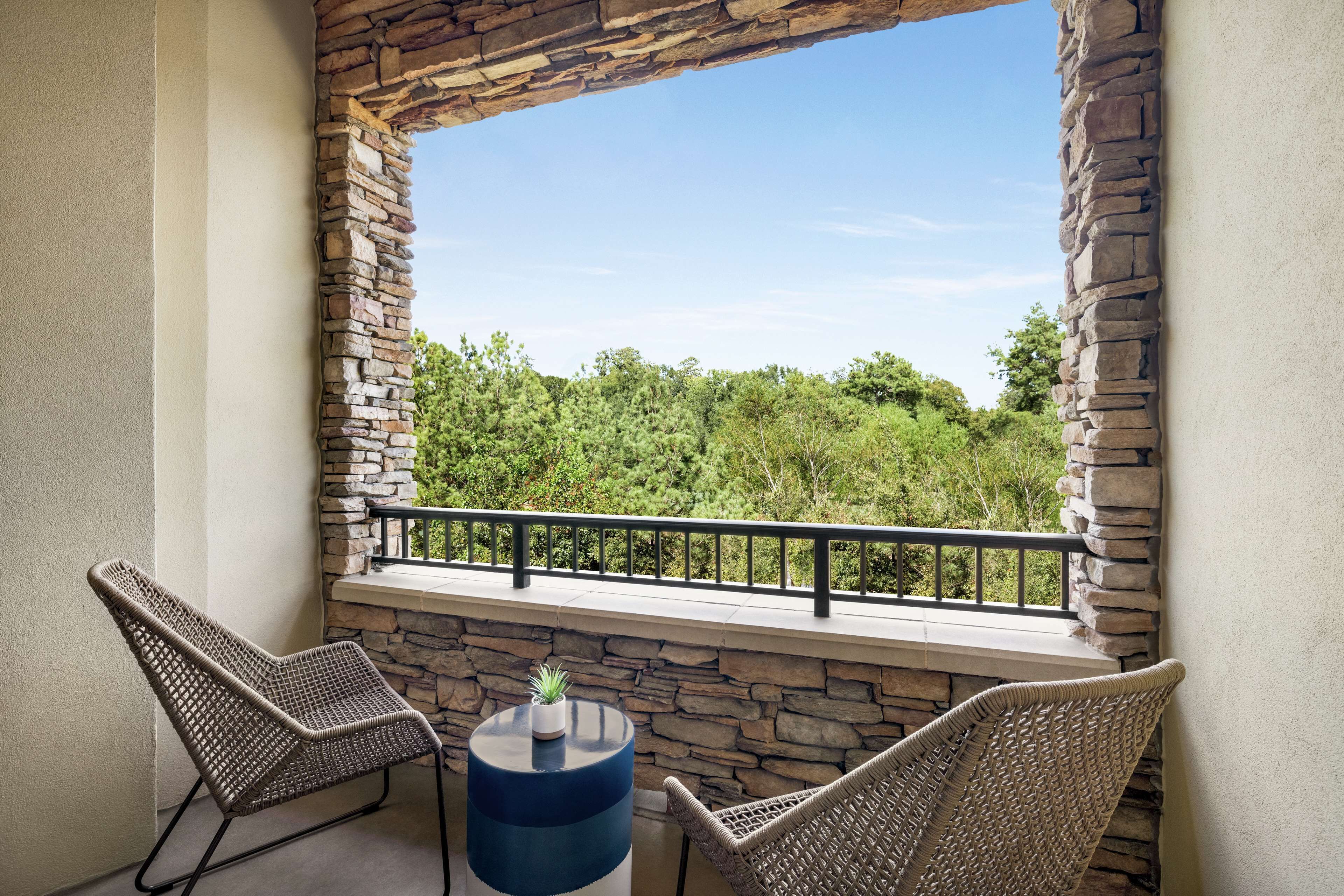 A balcony with stone walls, two wicker chairs, and a small table with a potted plant.