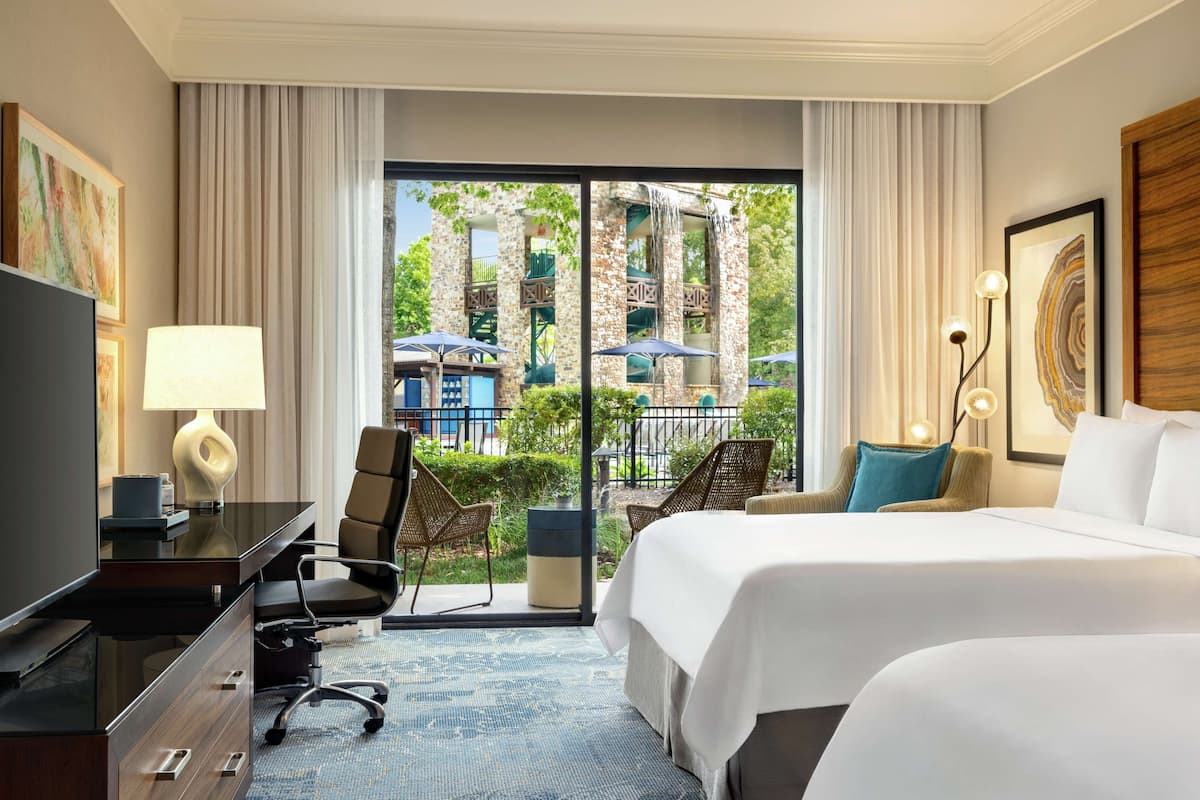 A hotel room with a bed, desk, chair, and a view of the outside.