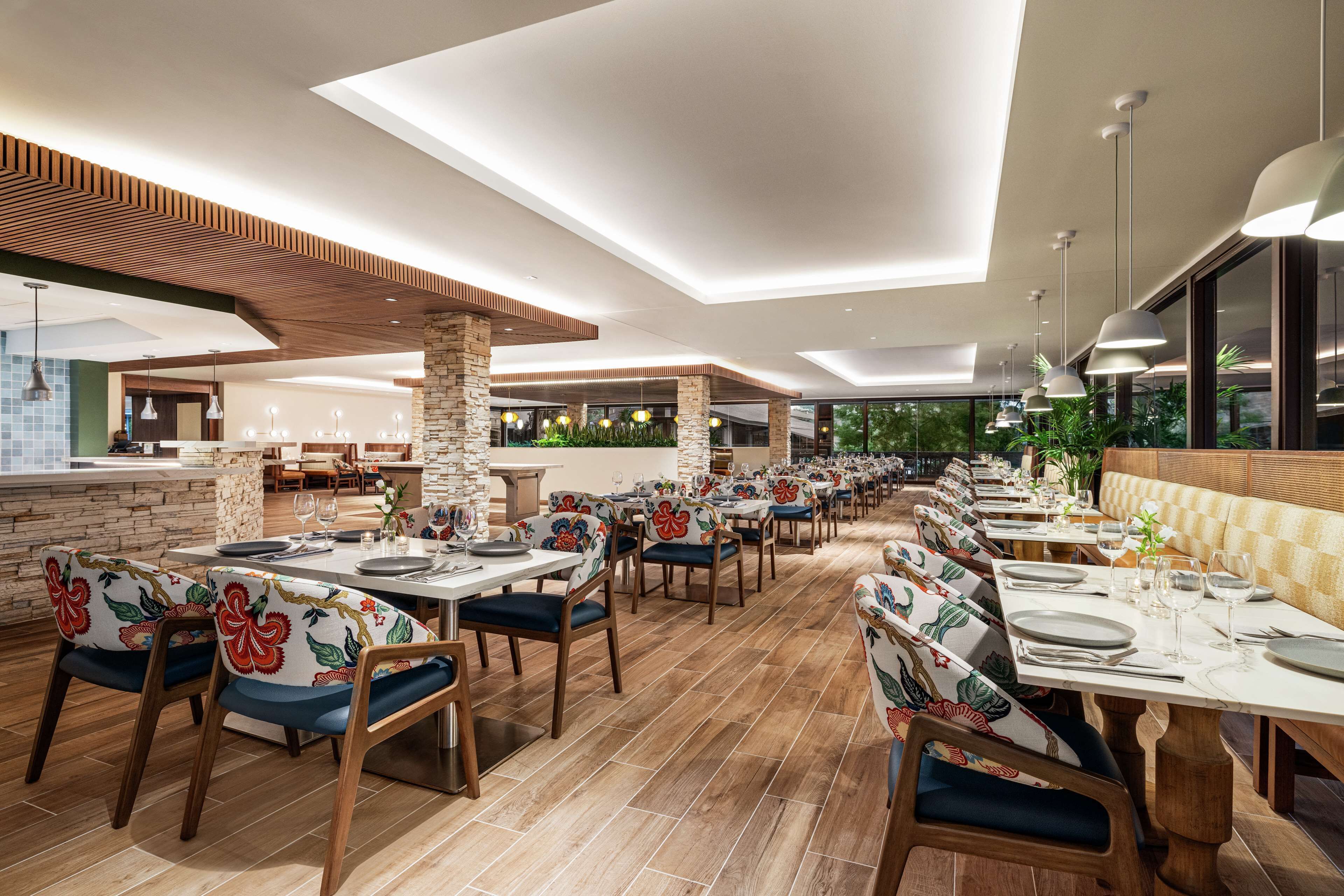 A spacious restaurant with high ceilings, wooden beams, and a long dining area with tables and chairs.