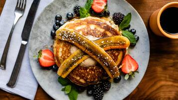 Un plat de crepes amb fruita i siroop, acompanyat d'una forquilla i un ganivet sobre un drap de taula.