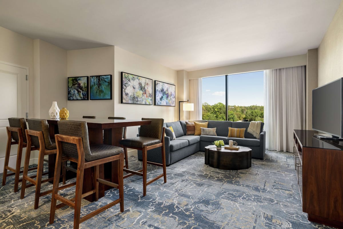 A modern hotel room with a dining area, a sofa set, a coffee table, and a TV.