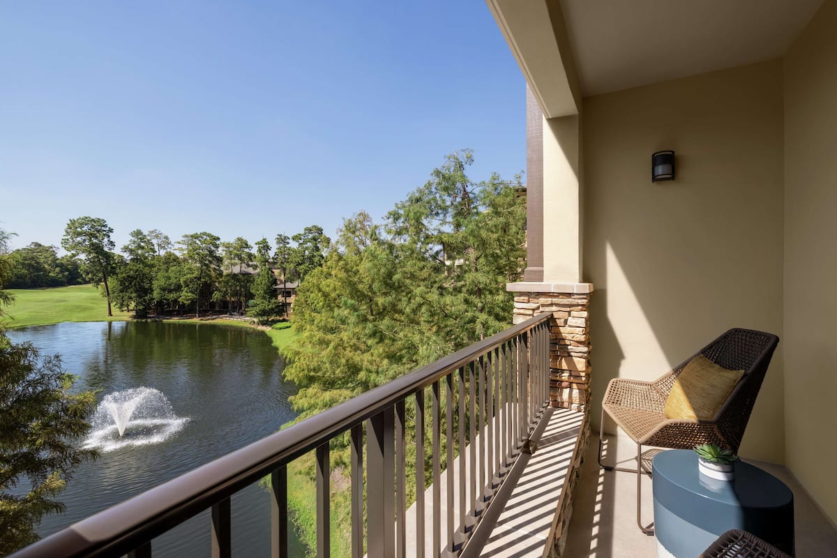 A balcony with a view of a lake, a fountain, and a golf course in the background.