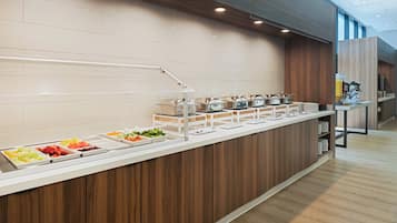 Uma área de buffet com diversas opções de comida, um canto de café e um design moderno com detalhes em madeira.