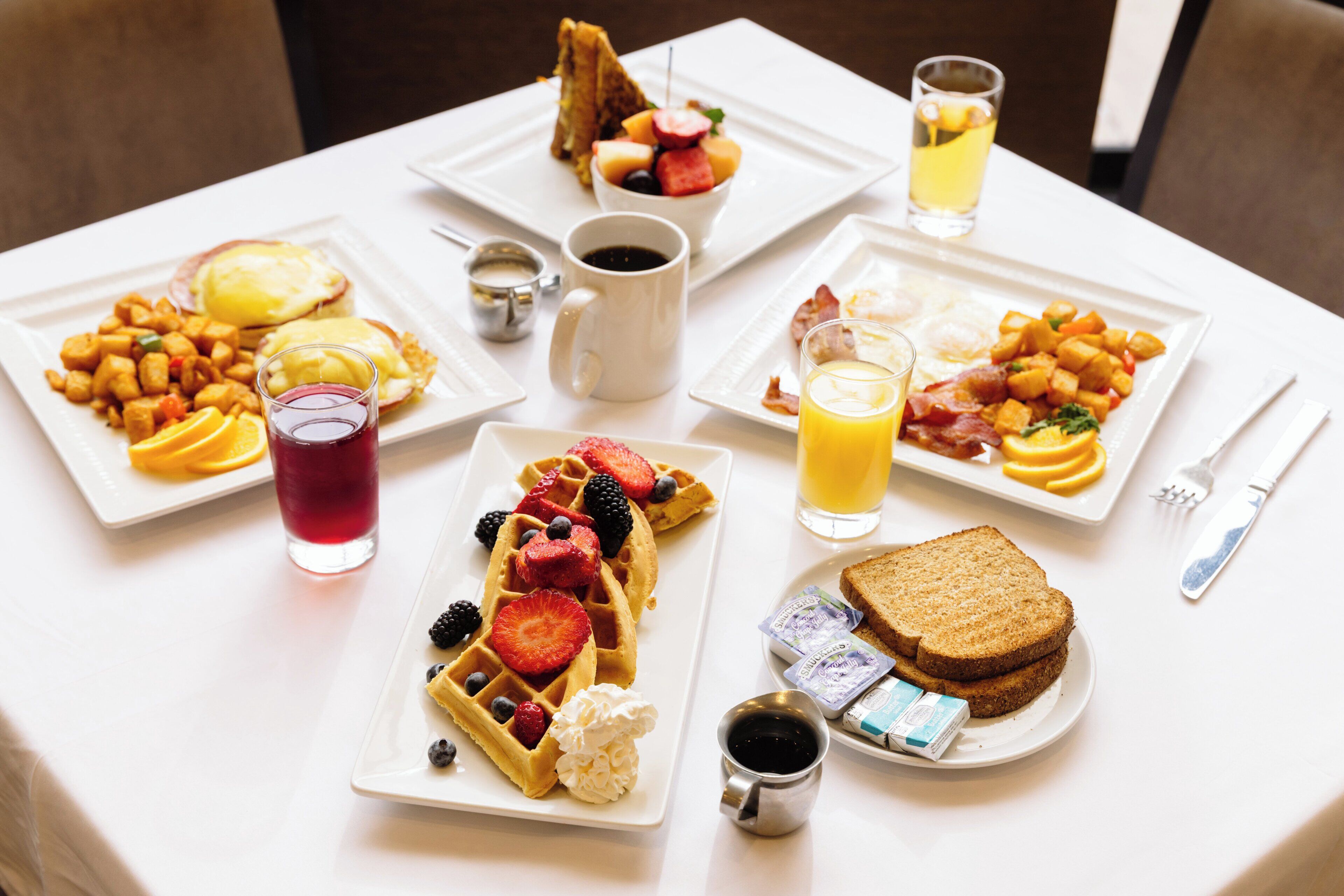 A breakfast table with various dishes including waffles, toast, and fruit.