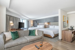 A hotel room with a sofa, two beds, a TV, and a wooden side table. - Holiday Inn Los Angeles Gateway - Torrance by IHG (Torrance)