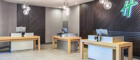 Una recepción con tres mostradores de madera, cada uno con un ordenador y un teléfono.