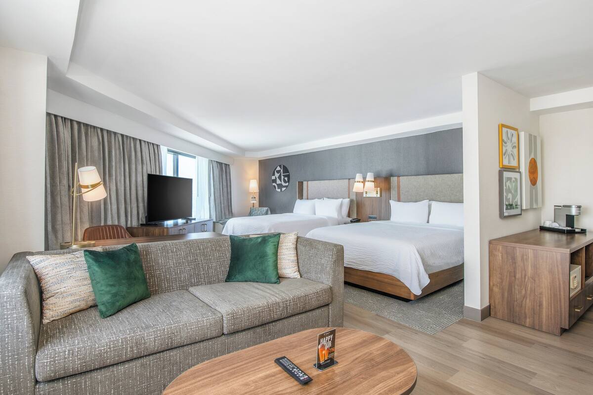 A hotel room with a sofa, two beds, a TV, and a wooden side table.
