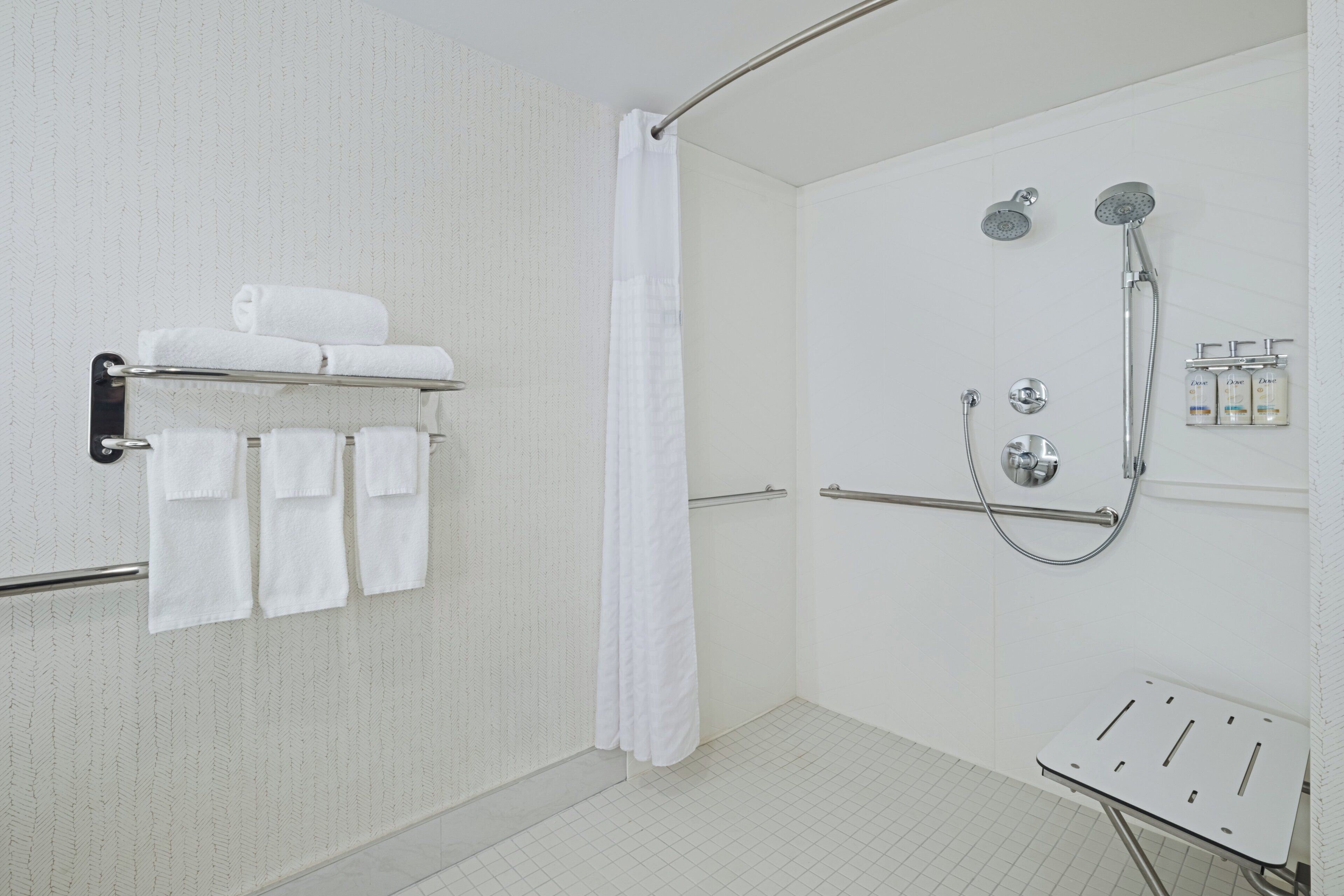 A shower area with a glass door, a towel rack with folded towels, a showerhead, and a handheld shower attachment.