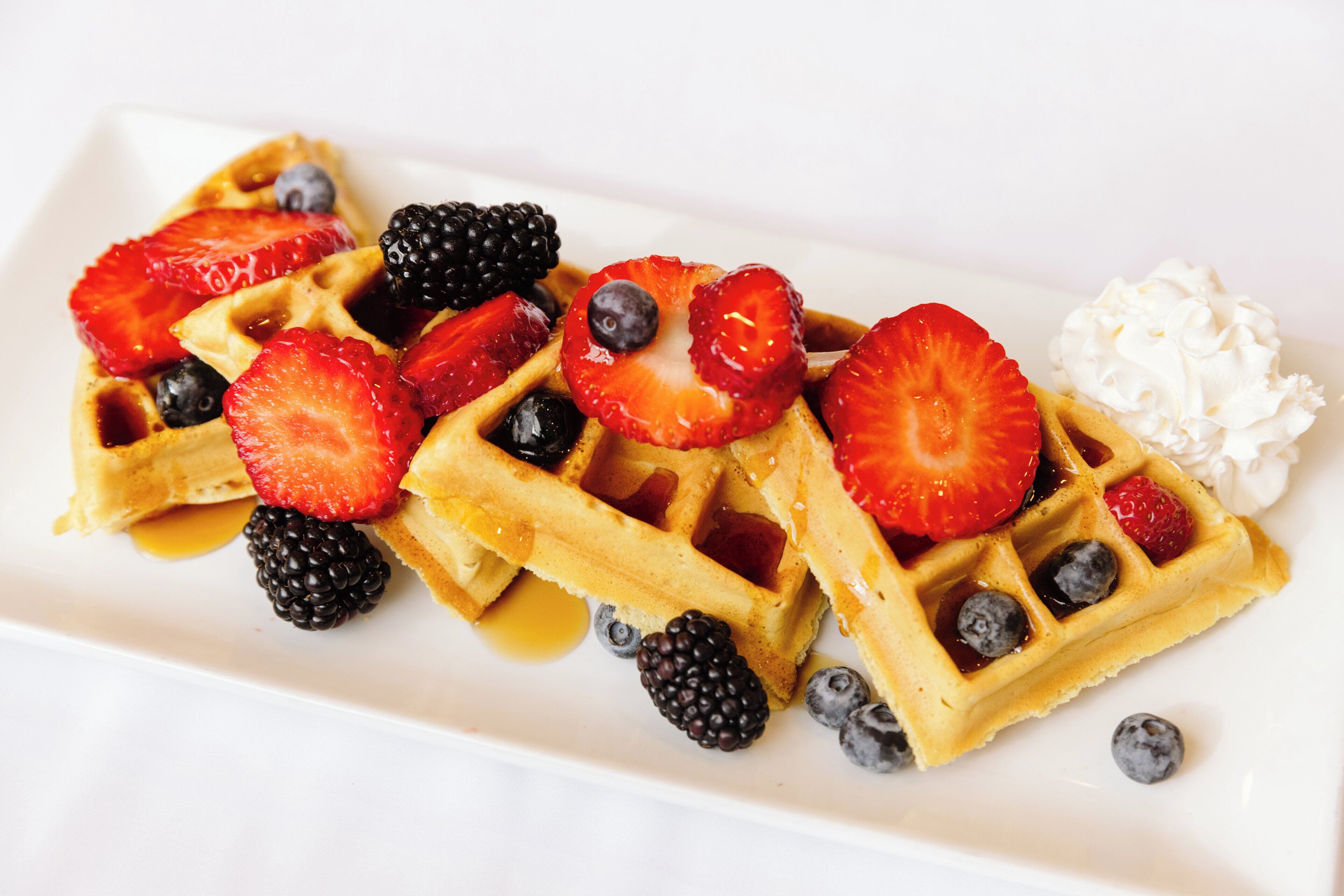 A plate of waffles topped with strawberries, blueberries, blackberries, and a dollop of whipped cream.