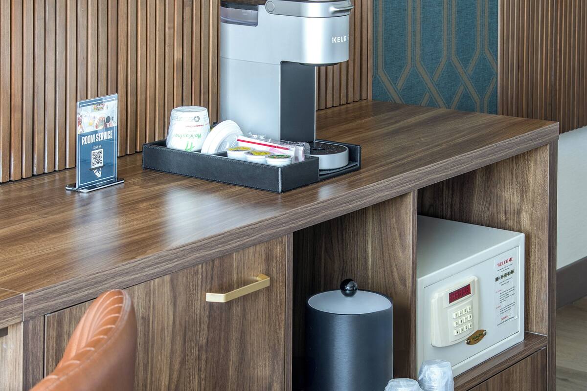 A coffee machine, a sign for room service, and a digital clock on a wooden counter.