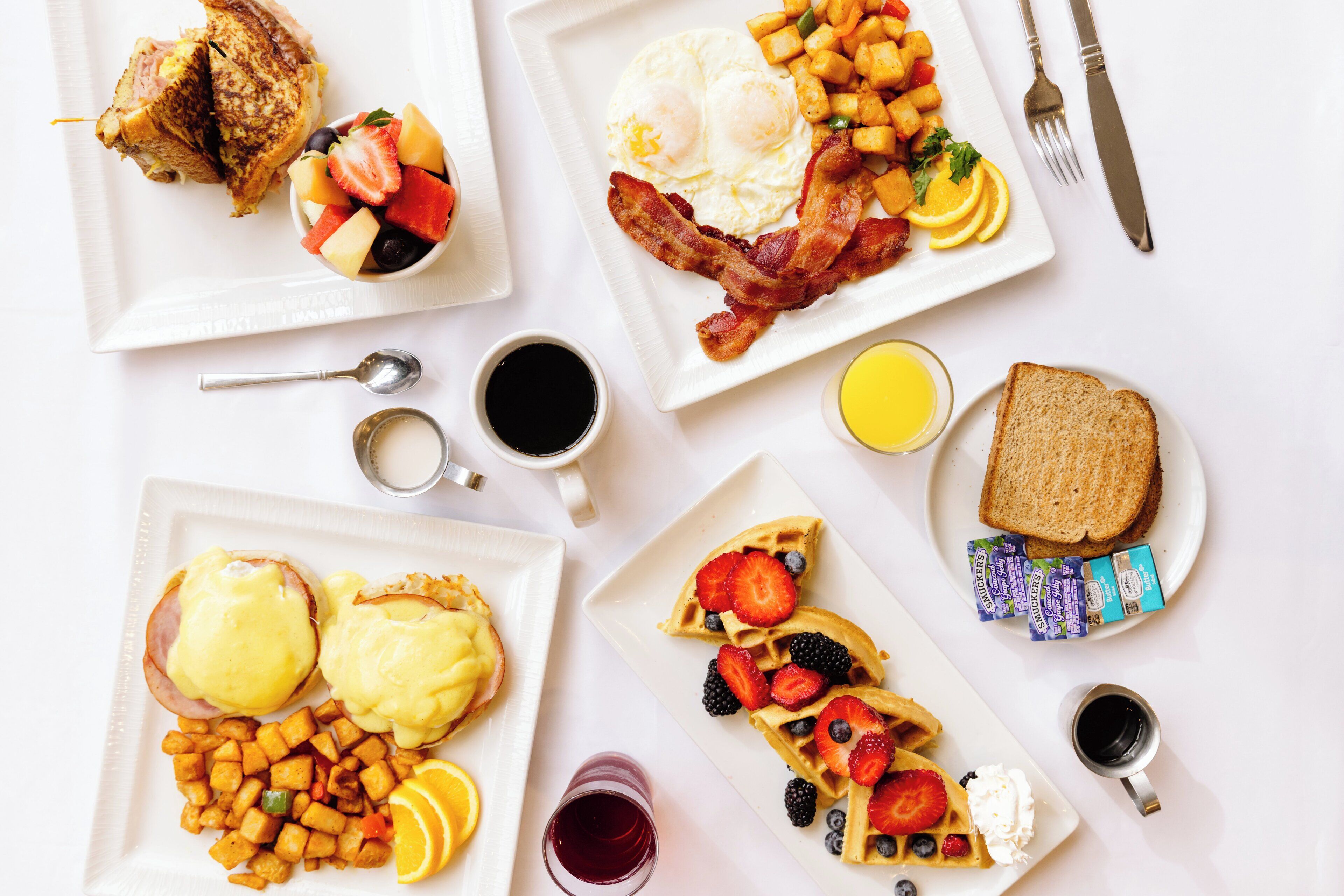 A breakfast buffet with various dishes including eggs, bacon, toast, waffles, and fruit.
