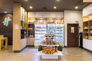Een moderne winkel met koelvitrines met de aanduiding 'eten' en 'drinken', en een etalage met verpakte producten in het midden.