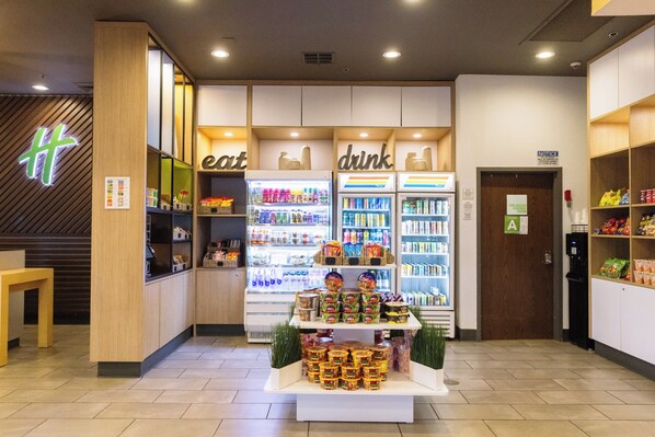 Uma loja de conveniência moderna com seções refrigeradas identificadas com 'comida' e 'bebida', e uma exposição de produtos embalados no centro.