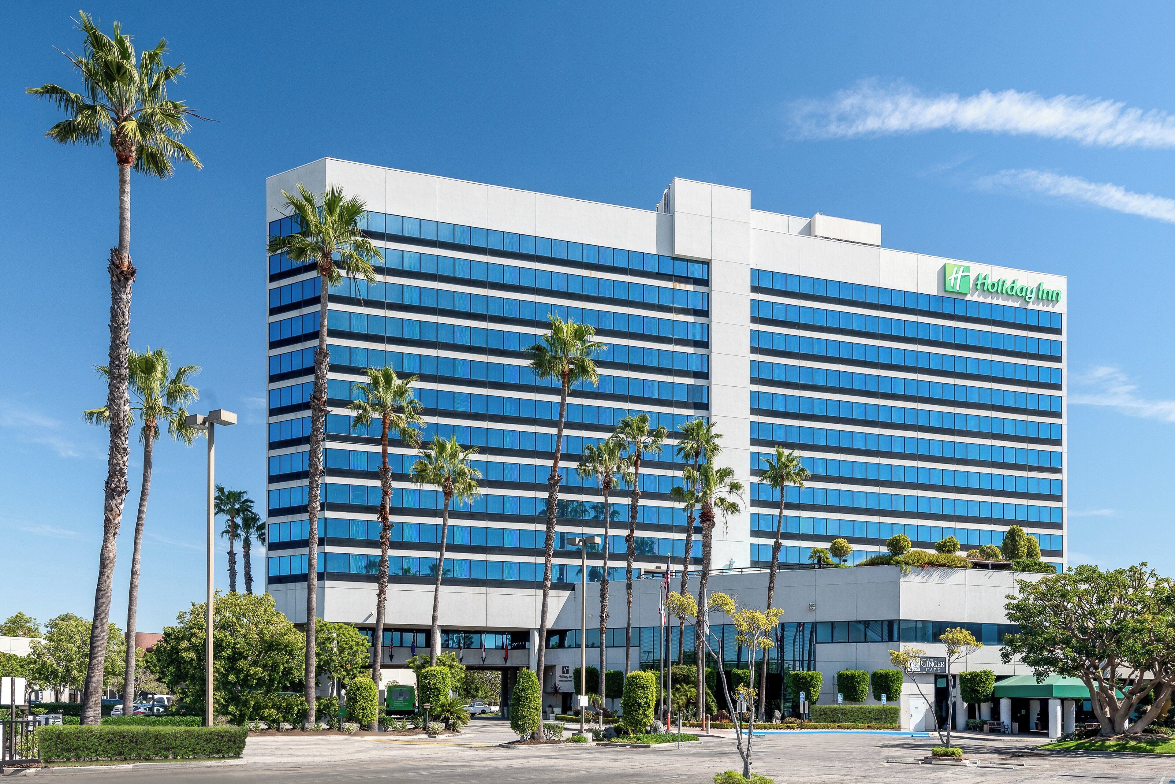 Un hôtel Holiday Inn à plusieurs étages, doté d’une façade moderne, avec une série de fenêtres et un logo vert bien visible.