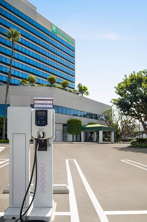 Een laadstation voor elektrische auto's op een parkeerplaats, met een Holiday Inn hotel op de achtergrond.