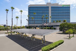 A Holiday Inn hotel with a parking lot featuring solar panels and palm trees.