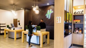 A reception area with wooden furniture, a counter, and a sign with a green cross. - Holiday Inn Los Angeles Gateway - Torrance by IHG (Torrance)
