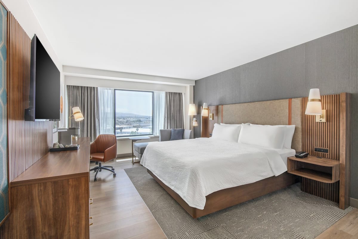 A modern hotel room with a large bed, a desk, a chair, and a TV.