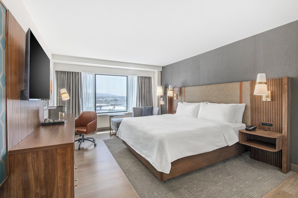 A modern hotel room with a large bed, a desk, a chair, and a TV.