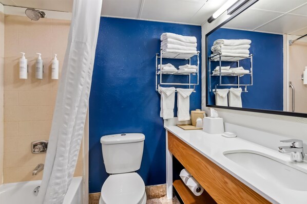A bathroom with a blue wall, white fixtures, a shower, a toilet, and a sink with a mirror.
