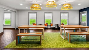 A modern room with wooden tables and benches, large windows with a view of greenery, and yellow pendant lights. - Spark by Hilton Wytheville Holston Rd I 81 (Wytheville)