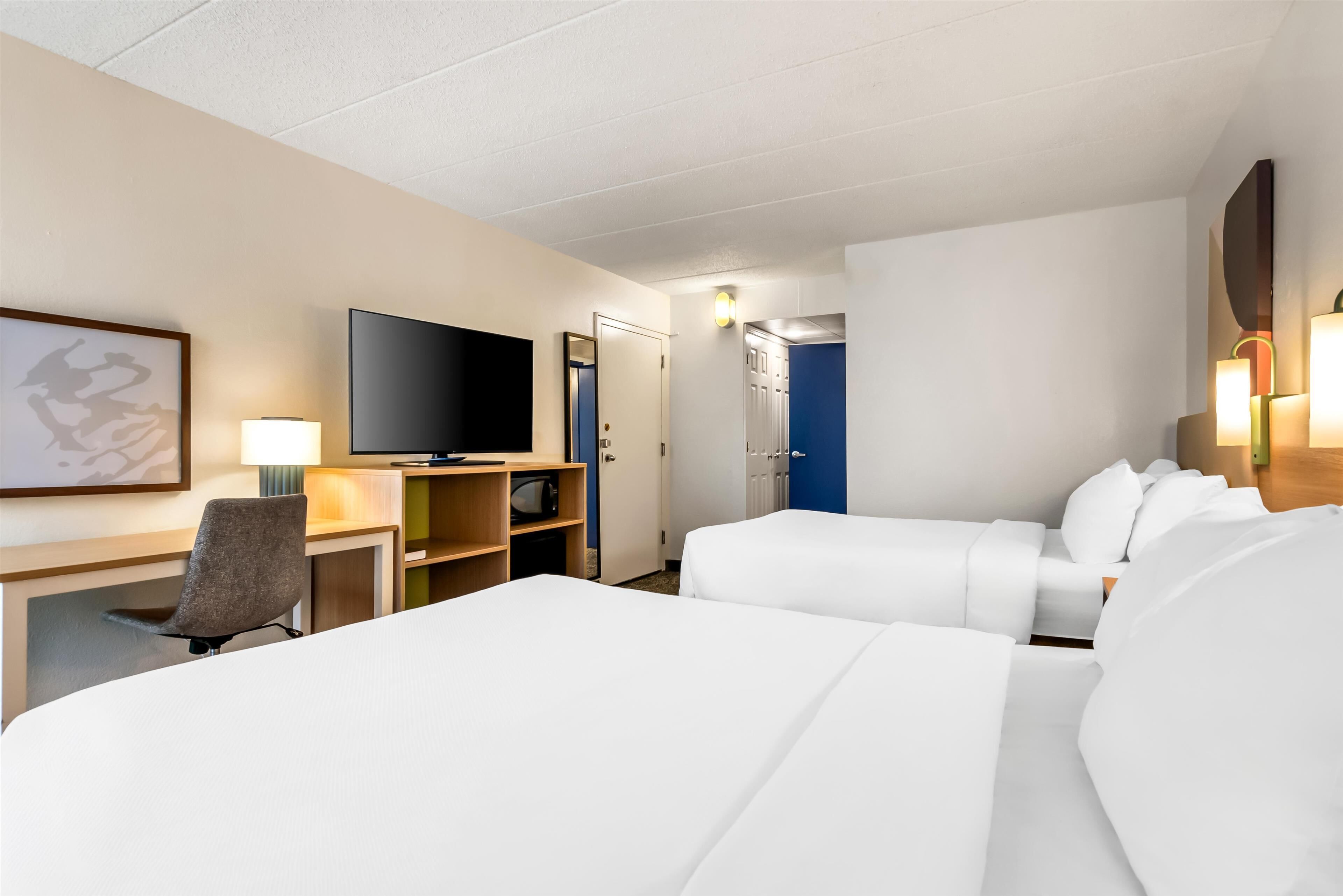 Una habitación de hotel con dos camas, un escritorio con una silla, un televisor y un armario.