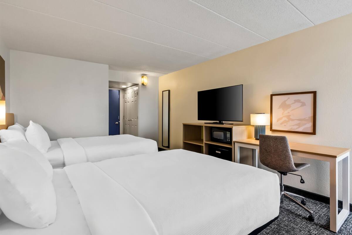 A hotel room with a large bed, a desk with a chair, a television, and a microwave.