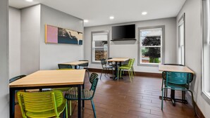 A dining area with multiple tables and chairs, a flat-screen TV mounted on the wall, and large windows providing natural light. - Spark by Hilton Wytheville Holston Rd I 81 (Wytheville)