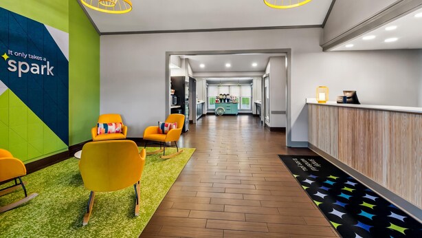 A modern reception area with a wooden reception desk, a green carpet, and yellow chairs. - Spark by Hilton Wytheville Holston Rd I 81 (Wytheville)