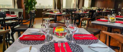 A restaurant with multiple tables set for dining, each with a bowl of fruit, wine glasses, and cutlery.