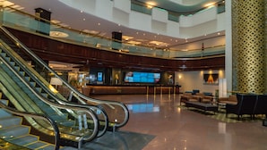 A spacious lobby with a central staircase, seating area, and a large digital display.