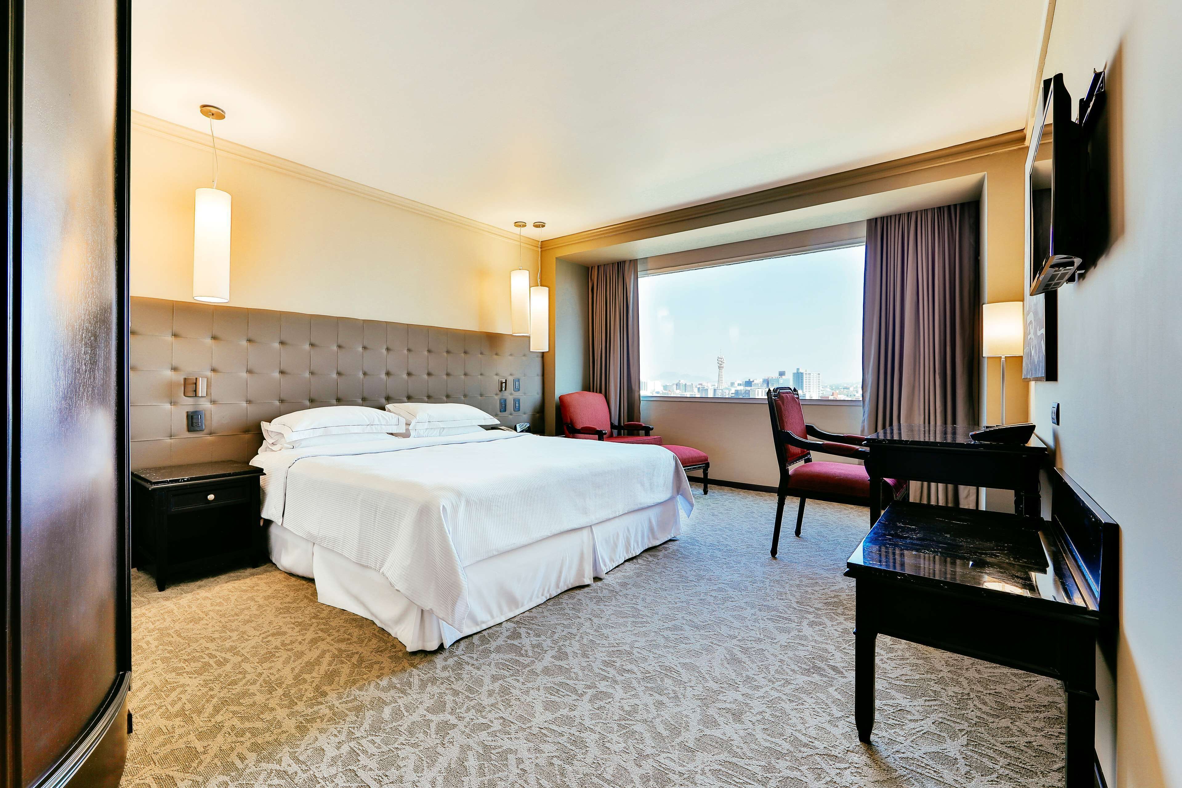 Een hotelkamer met een bed, een bureau, een stoel, een televisie en een raam met uitzicht op de stad.