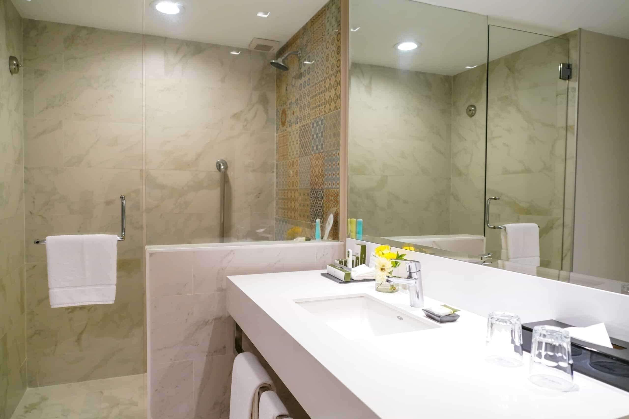 A modern bathroom with a large mirror, a bathtub, a shower, and a vanity with a sink and toiletries.