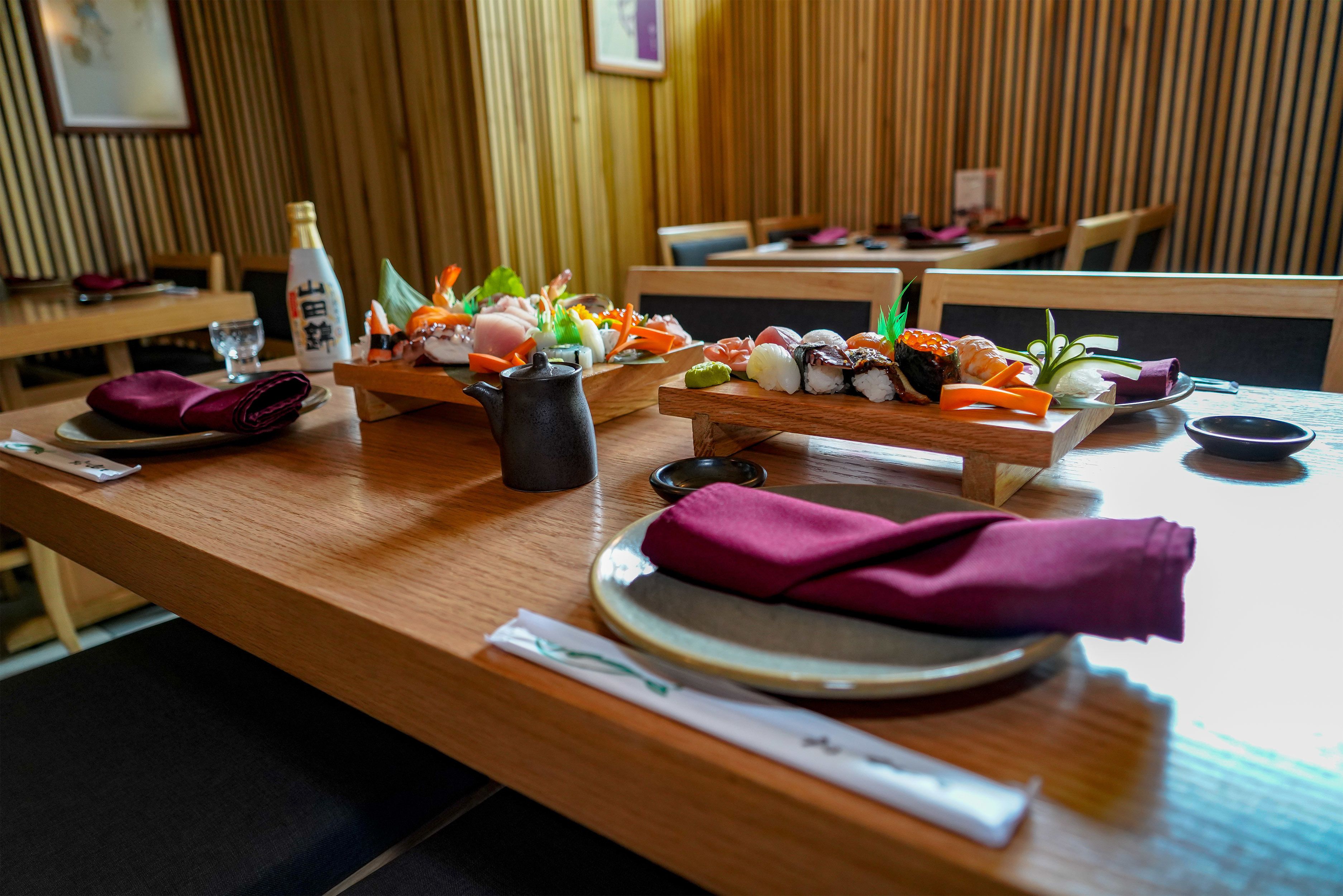 A restaurant interior with wooden paneling, sushi platters, a bottle, and a teapot on the table.