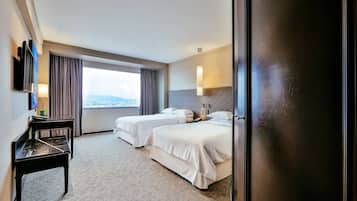 A hotel room with two beds, a desk, a TV, and a large window with a view.