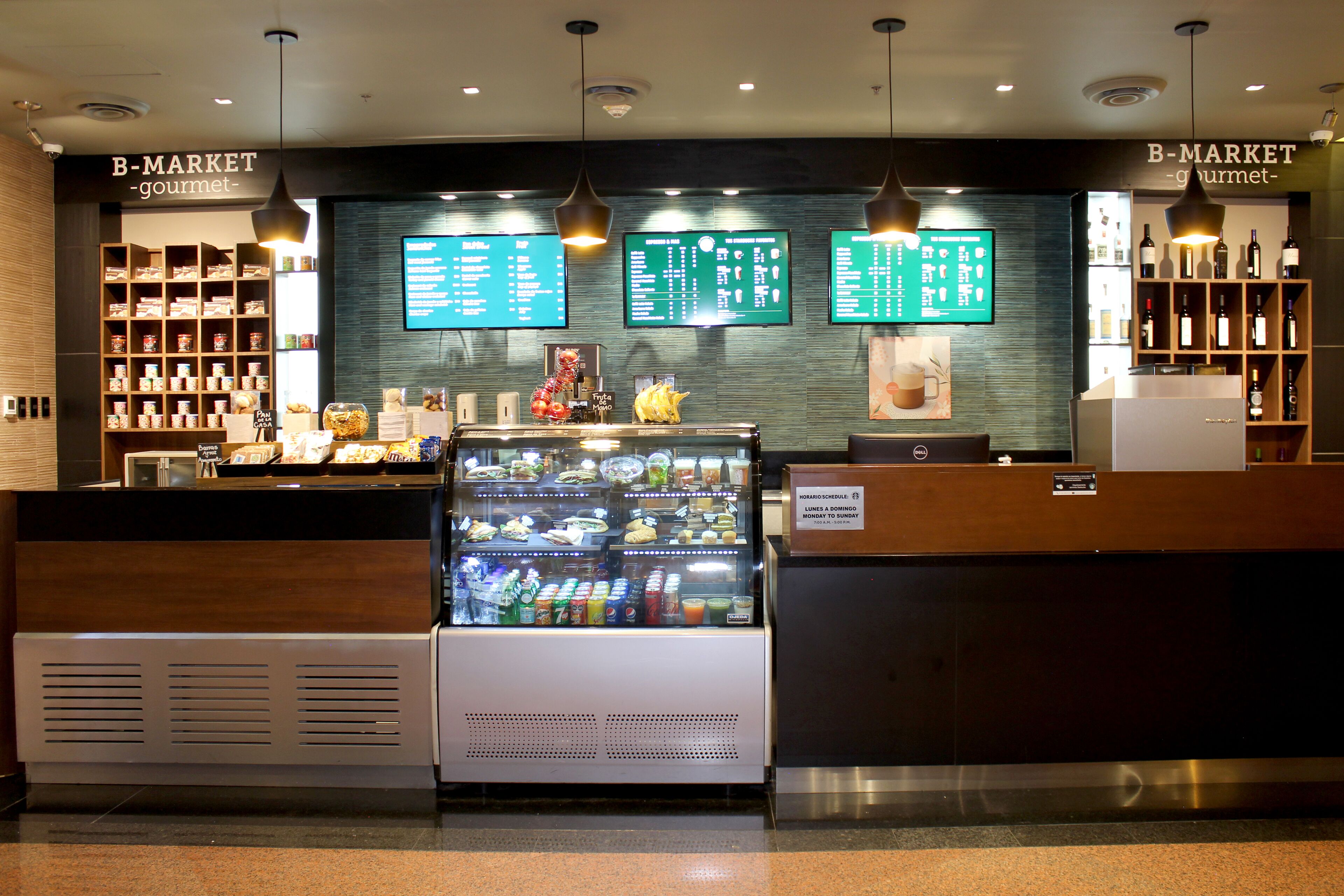 A B-Market gourmet food counter with a refrigerated display, menu boards, and shelves of snacks and beverages.