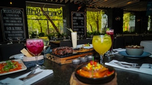 A restaurant with a variety of dishes and drinks on the table, including a large bowl of soup and a plate of grilled meat.